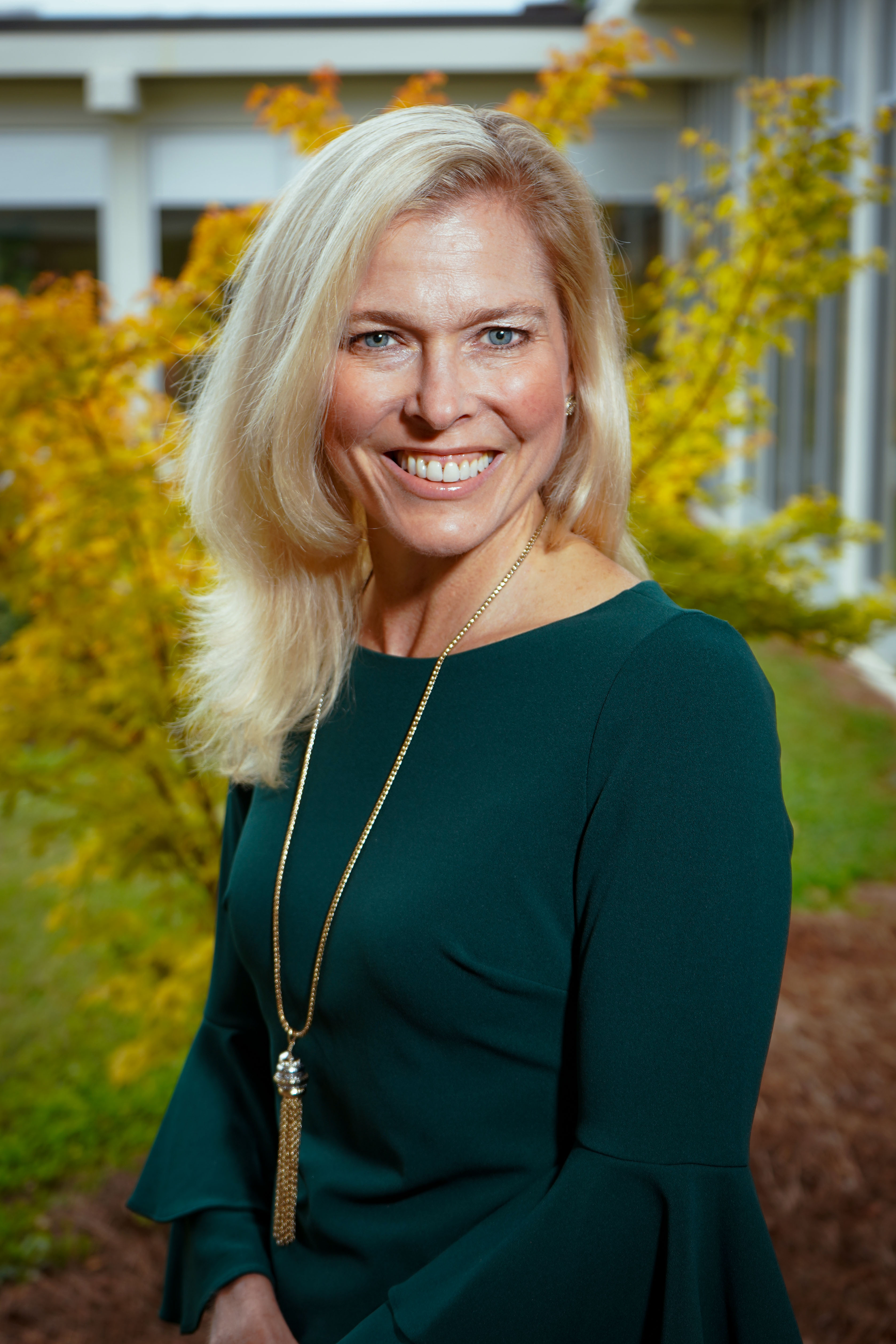 A blonde woman in a green dress and gold necklace.