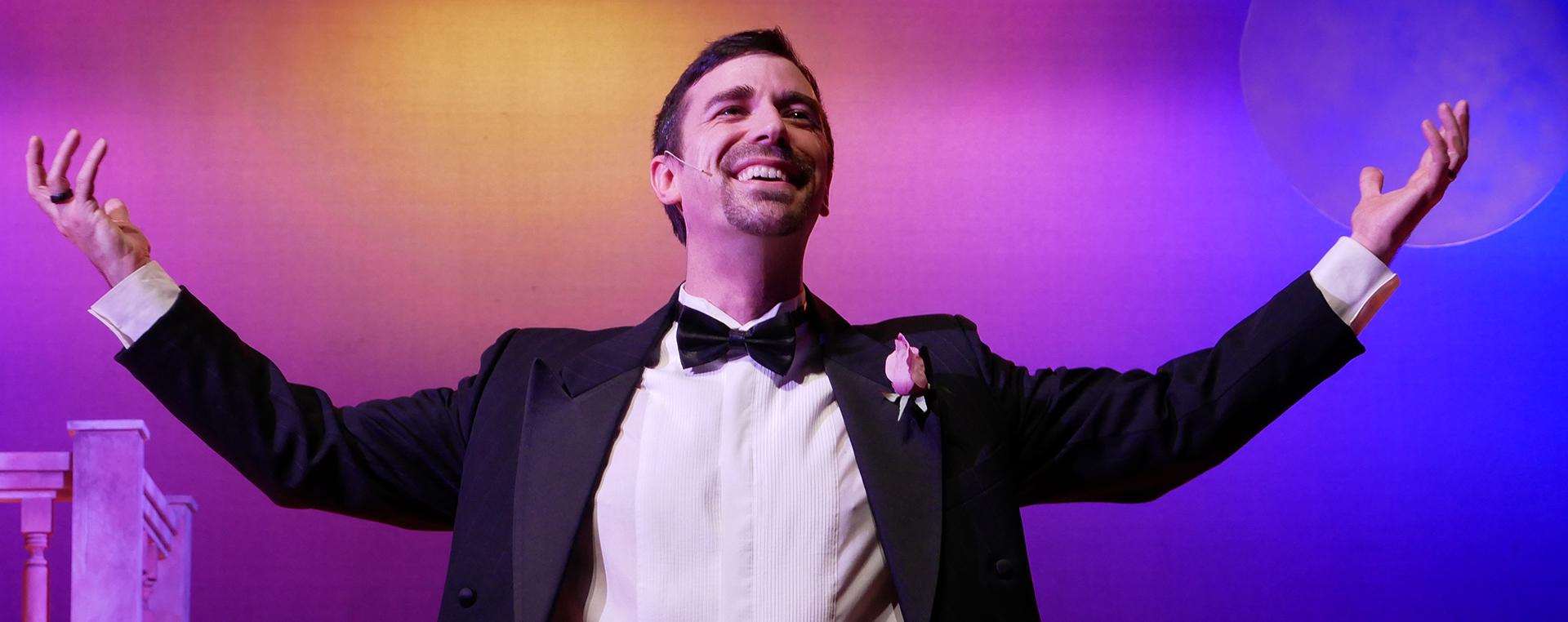 a smiling man in a tuxedo with his arms raised