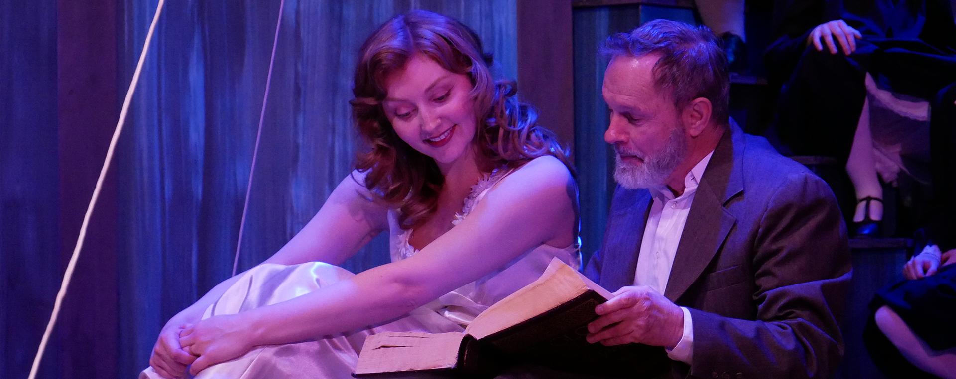 a seated older man reading a book to an also seated younger woman