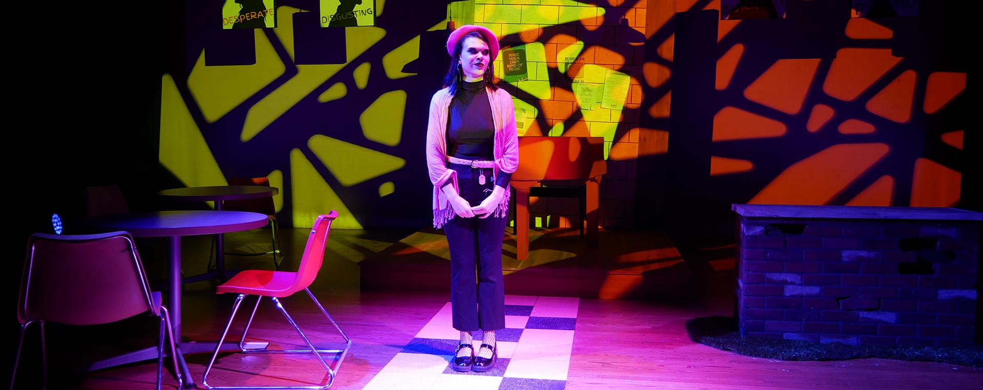 an actress standing center stage amidst strong shadows and pink lighting