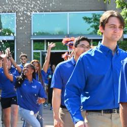 Students in Blue SkillsUSA shirts queue to board a bus to Atlanta. In the background, two young women reach for bubbles in the air as they celebrate.