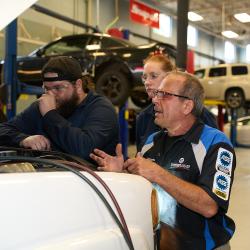 An instructor and two students look under the hood of a car.