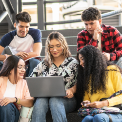 Stock photo of five college-aged students sitting on stairs looking at a laptop. Stock photo of five college-aged students sitting on stairs looking at a laptop.