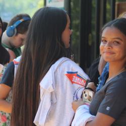 A brunette woman looks into the camera with several people standing behind her holding tee shirts.