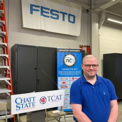 Student John Jordan stands in front of a lectern and signage for ChattState, TCAT, and industry partners.