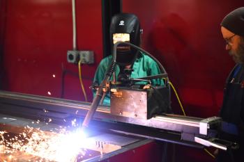 A young woman and an instructor look on at a welding machine.