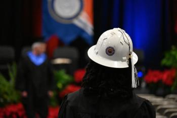 Graduation 2025 A woman with black curly hair walks down a graduation aisle wearing a hard hat.