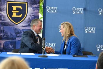 BlueHorizon Transfer A man in a suit shakes the hand of a woman in a suit in front of ETSU and ChattState backdrops.