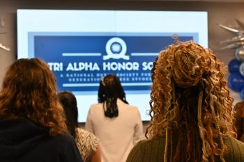 Women in focus look on at an out-of-focus sign that reads "Tri-Alpha Honor Society"