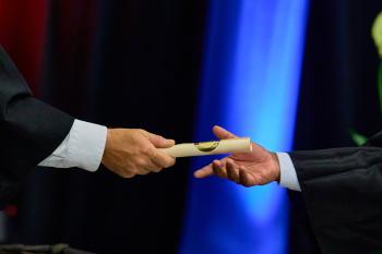 A close up of one person handing a diploma to another person.