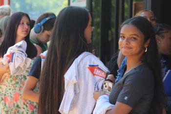 A brunette woman looks into the camera with several people standing behind her holding tee shirts.